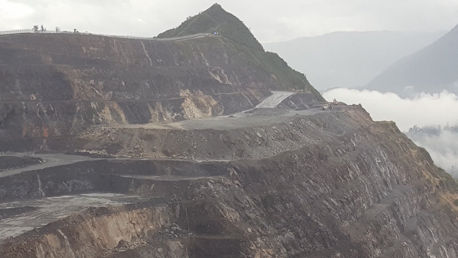 Cut back benches of the Porgera open pit mine in Papua New Guinea, with cloud sitting below the pit rim.
