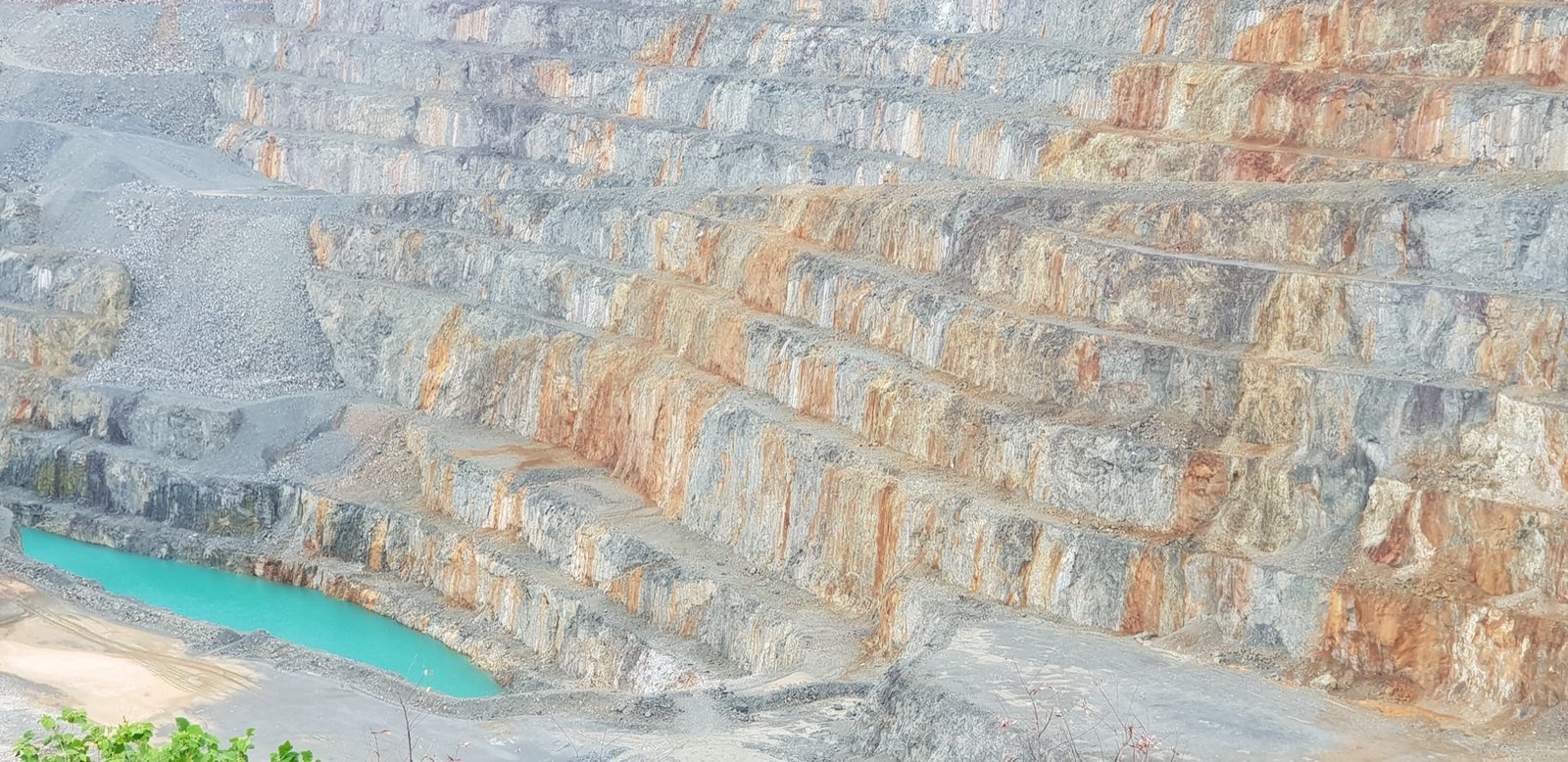 Presplit benches on an open pit highwall, with a turquoise pit lake at the toe.
